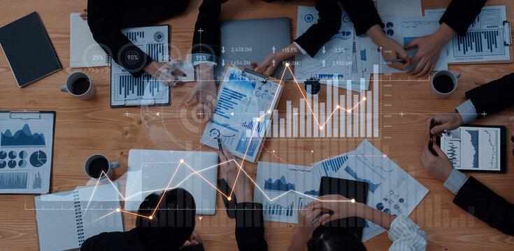 A diverse group of business professionals engage in a collaborative meeting, analyzing charts and data on tablets and documents to drive strategy and performance insights. Scalp