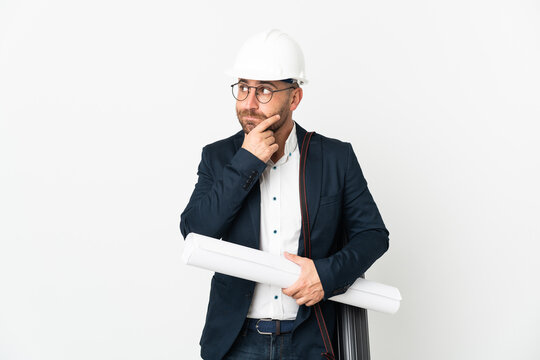 Architect man with helmet and holding blueprints isolated on white background having doubts and thinking