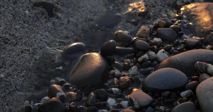 Zen pebble stones on the foreshore of small trickling beach stream lit by the golden light of the setting sun during a peaceful sunset golden hour.  4K natural landscape  