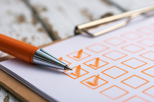 An orange pen rests on a clipboard with checkboxes filled with orange checkmarks on a rustic wooden desk. This business survey concept is perfect for quality control and.