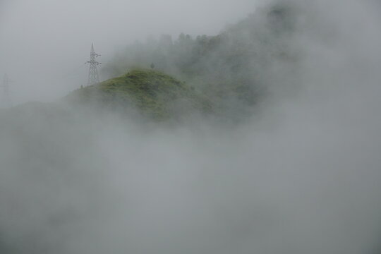Heavy morning mist engulfing a steep green hillside featuring a high-voltage transmission tower.