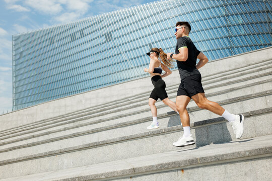 Running duo navigating steps with energy in a modern urban landscape under a bright blue sky