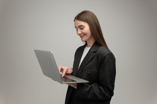 Smiling woman enjoys technology while typing on laptop in stylish black suit
