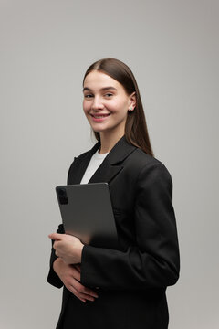 Young professional woman in a sleek suit holds a tablet while smiling confidently against a neutral backdrop