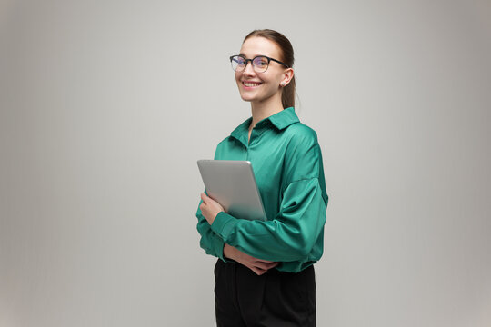Young woman in a green blouse holds a tablet and smiles with confidence in a modern studio setting