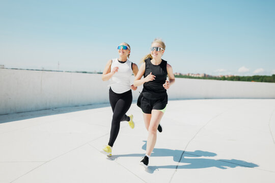 Two women enjoying a sunny day while jogging on a modern rooftop track with blue skies above