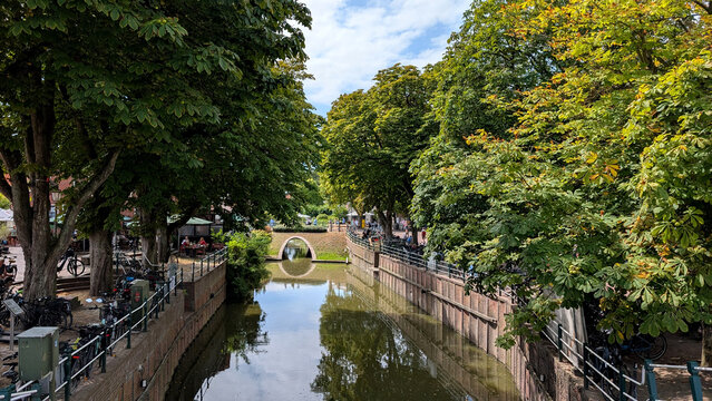 Tree-lined canal with small bridge in Greetsiel, Germany. 
