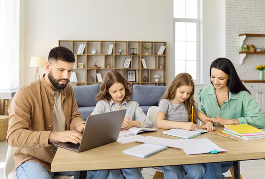 Family parents and children studying homework at home. Parents guide two daughters with pencils, while father works on a laptop at home learning. Clear concept of family education support