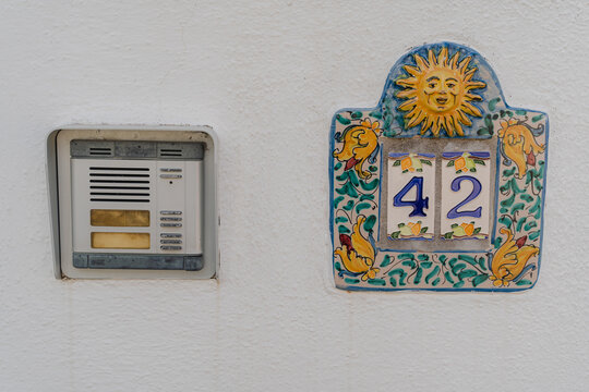Decorative ceramic house number sign mounted on white exterior wall.