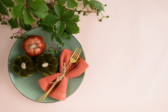 Elegant Thanksgiving table setting with decorative pumpkins, golden cutlery, and autumnal foliage on a pastel background
