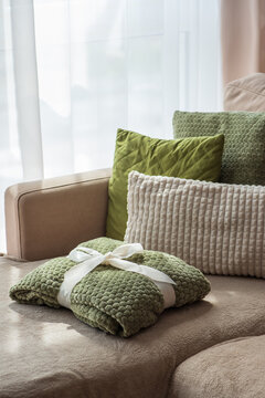 Cozy green blanket tied with white ribbon resting on comfortable sofa with plush pillows