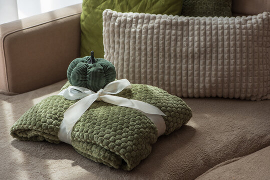 Cozy Green Textured Throw Blanket Tied With White Ribbon And Decorative Pumpkin On Sofa With Pillows