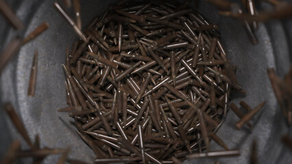 Pile of spent bullet casings in a metal container, surrounded by scattered casings under dim lighting with metallic sheen and rust stains. © Piotr Adamczyk