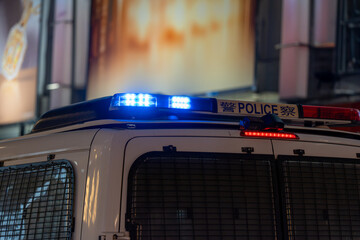Top angle close-up of blue LED emergency lights active on the roof of a municipal police vehicle in an urban setting. © Sergej