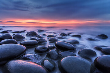 Fototapeta premium Round black stones on a calm sea shore at twilight
