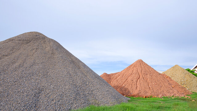 Large piles of gravel, crushed stone, and sand in industrial site or building supply yard under blue sky
