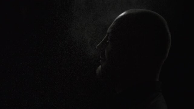 Man raising his head as water droplets rise in dark atmosphere