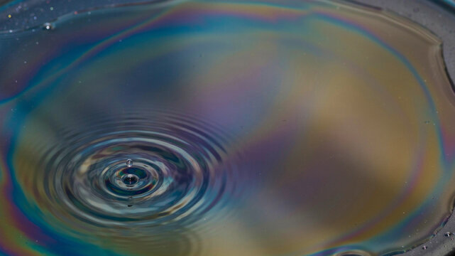 Iridescent Swirls: A close-up view of an iridescent oil slick on water, creating a mesmerizing pattern of rainbow colors with concentric ripples from a water drop.