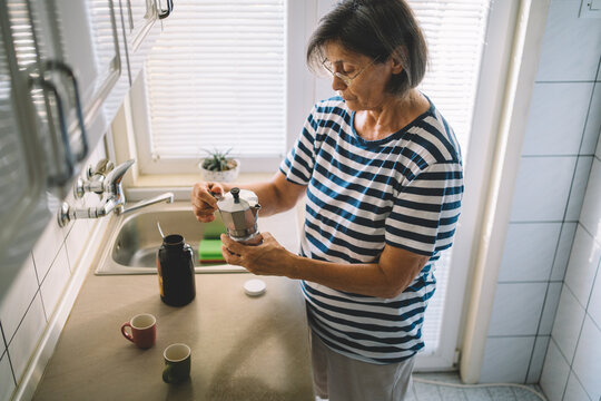 Elderly woman preparing coffee with moka pot in kitchen