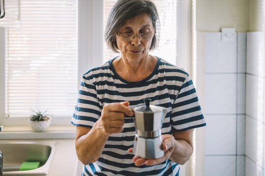 Older woman holding moka pot during coffee preparation