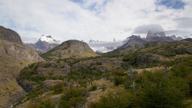 Panoramic view of Patagonia wilderness: rocky mountains, green forests, and snow-capped peaks of El Chalt&eacute;n under a cloudy sky