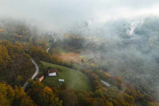 Drone shot of fog rolling over autumn hills and a small rural house in a mountain valley