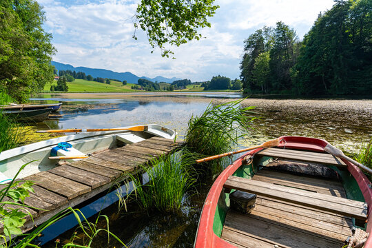 Ruderboot an einem h&ouml;lzernen Steg am Ufer eines ruhigen Sees.