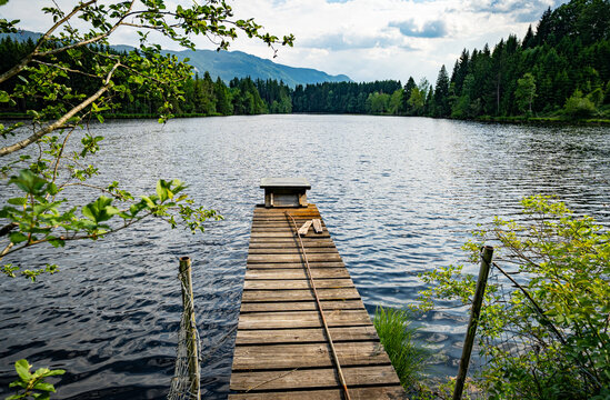 Schmaler Holzsteg f&uuml;hrt auf einen ruhigen Waldsee in den Alpen.