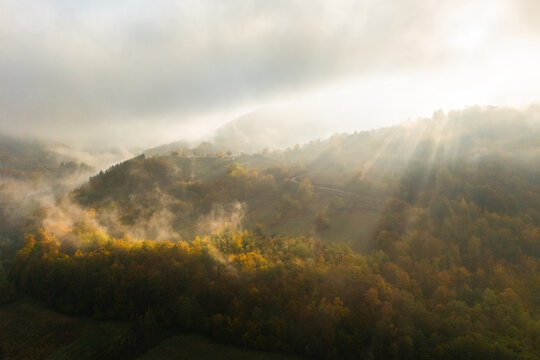 Aerial view of mountain forests shrouded in morning mist with dramatic sunbeams breaking through the clouds