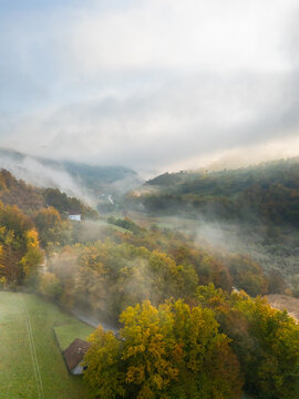 Drone shot of fog rolling over autumn hills and a small rural house in a mountain valley