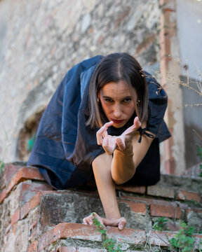 Woman in Cape Crouching and Reaching on Rustic Brick Wall