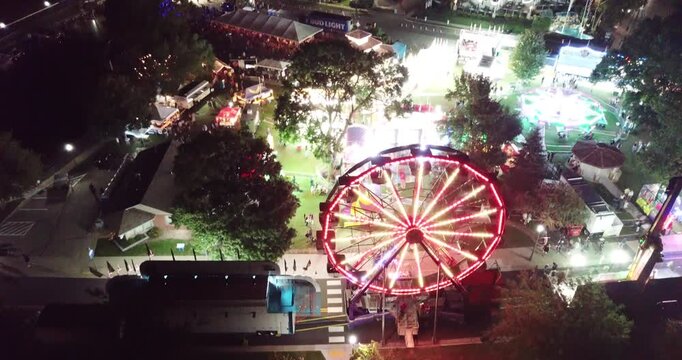 Aerial drone video flying slowly tilting down in front of ferris wheel and amusement rides with lots of lights at a carnival in Lake Geneva, Wisconsin.