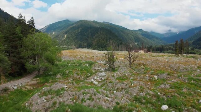 Dramatic aerial photography flying over the remnants of a devastating landslide in Georgia's remote Shovi Racha mountain valley, revealing a wide path of rocks and debris among lush green coniferous f