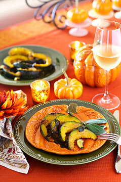 Roasted pumpkin Kabocha squash with sage in a fall table setting with orange and green plates 