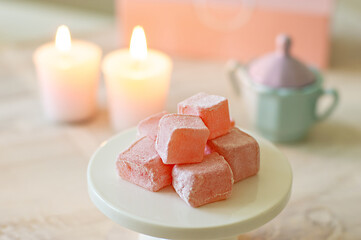 Fototapeta premium Cubes of rose Turkish delight candy in a pastel setting with candles 