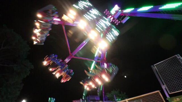 An amusement ride swinging back and forth at night with all the lights lit up at a carnival.