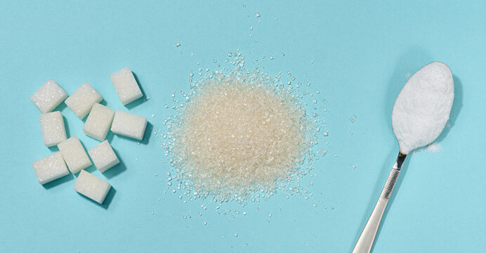 Three types of refined sugar in cubes, loose cane sugar and powdered sugar in a spoon