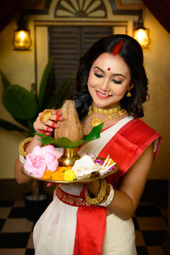 Portrait of beautiful Indian woman wearing traditional red and white saree and jewellery, holding a plate of religious offerings