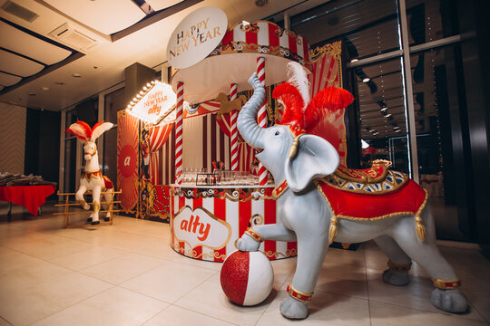 Carnival Celebration: A festive carnival stall decorated with red and white stripes features a whimsical elephant statue holding a ball, and a carousel horse in the background.
