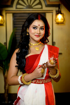 Portrait of beautiful Indian woman wearing traditional red and white saree and jewellery, holding Rudraksha mala in her hand