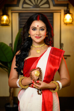 Portrait of beautiful Indian woman wearing traditional red and white saree and jewellery, holding Rudraksha mala in her hand