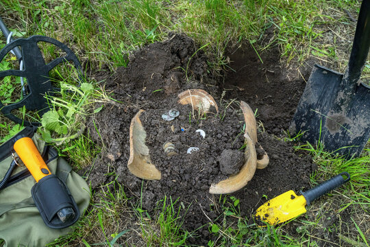 A metal detector and tools to dig for treasure in the ground. They found some coins and pottery among the ground. The activity takes place on a grassy area