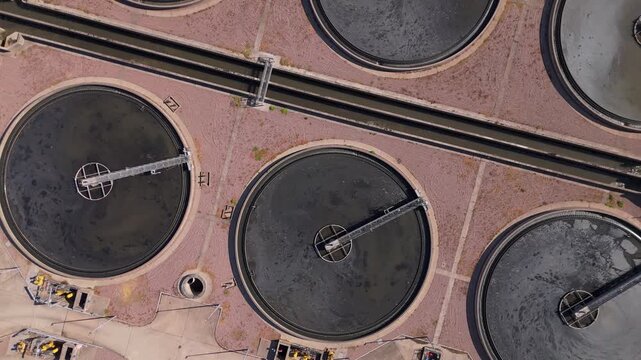 Aerial drone view straight down and rising over clarifier tanks at a large waste water treatment plant in Minworth, UK