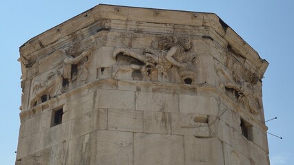 Roman Agora, Athens, Greece - 8 July 2026. Close view of three wind deity reliefs carved beneath the cornice of the Tower of the Winds. © Michael