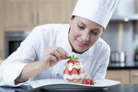 Female chef decorating strawberry dessert with mint leaf
