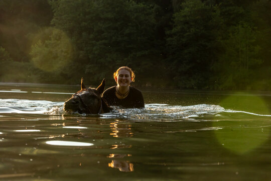 Reiterin badet mit Pferd im Gegenlicht