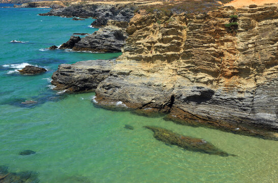 Clear turquoise shallow water of a secluded beach and steep cliffs, in Porto Covo, a growing tourist resort on Portugal's west coast. Sines, Alentejo, Portugal.