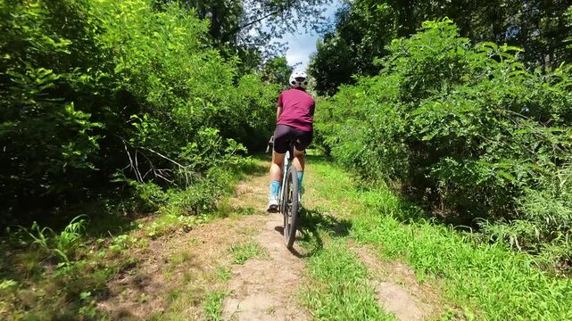 Woman rides a gravel bike along a narrow trail through dense green vegetation. Active cycling concept suits adventure, fitness, travel and outdoor lifestyle themes