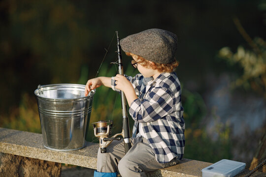 Blonde curly boy sitting on a bench and holding a fishing rod