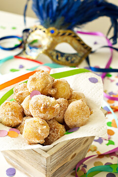 Italian Carnival Fritters in a wood basket with colorful confetti, streamers and a carnival mask 